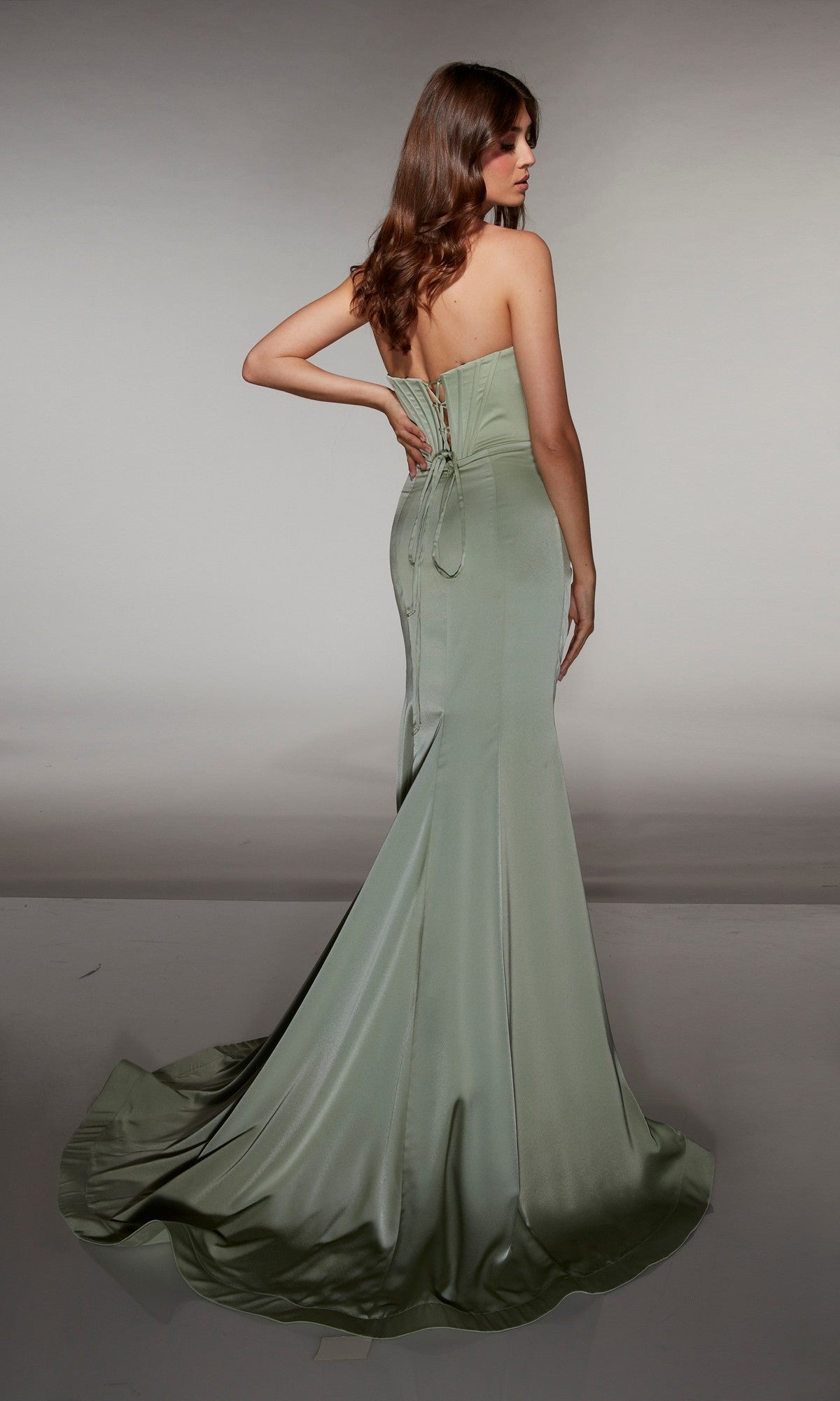 A woman stands facing away, looking over her shoulder in the Alyce 62062—a long strapless satin prom dress with a lace-up corset bodice.